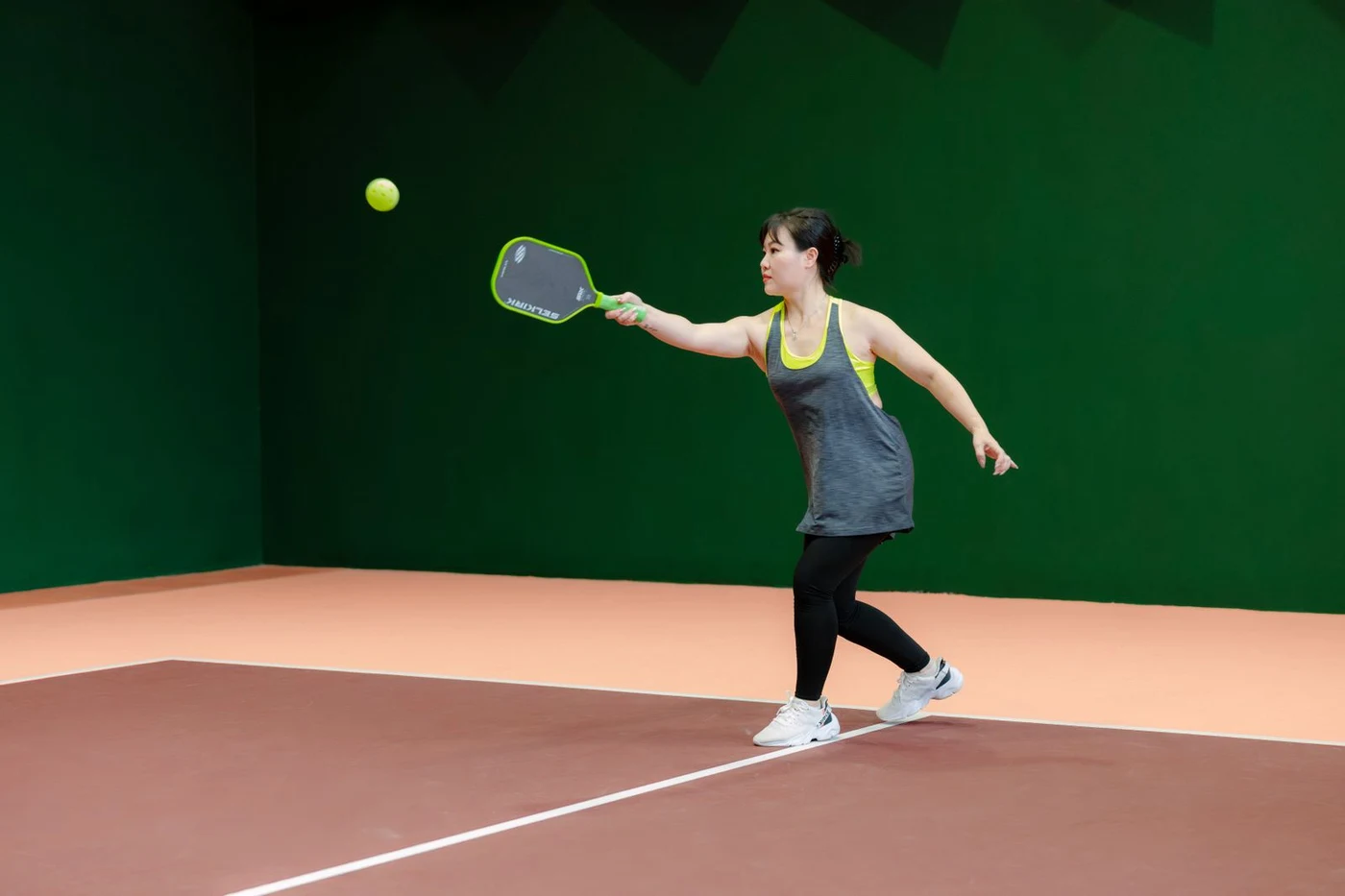 A player stretching for a forehand return on an indoor pickleball court
