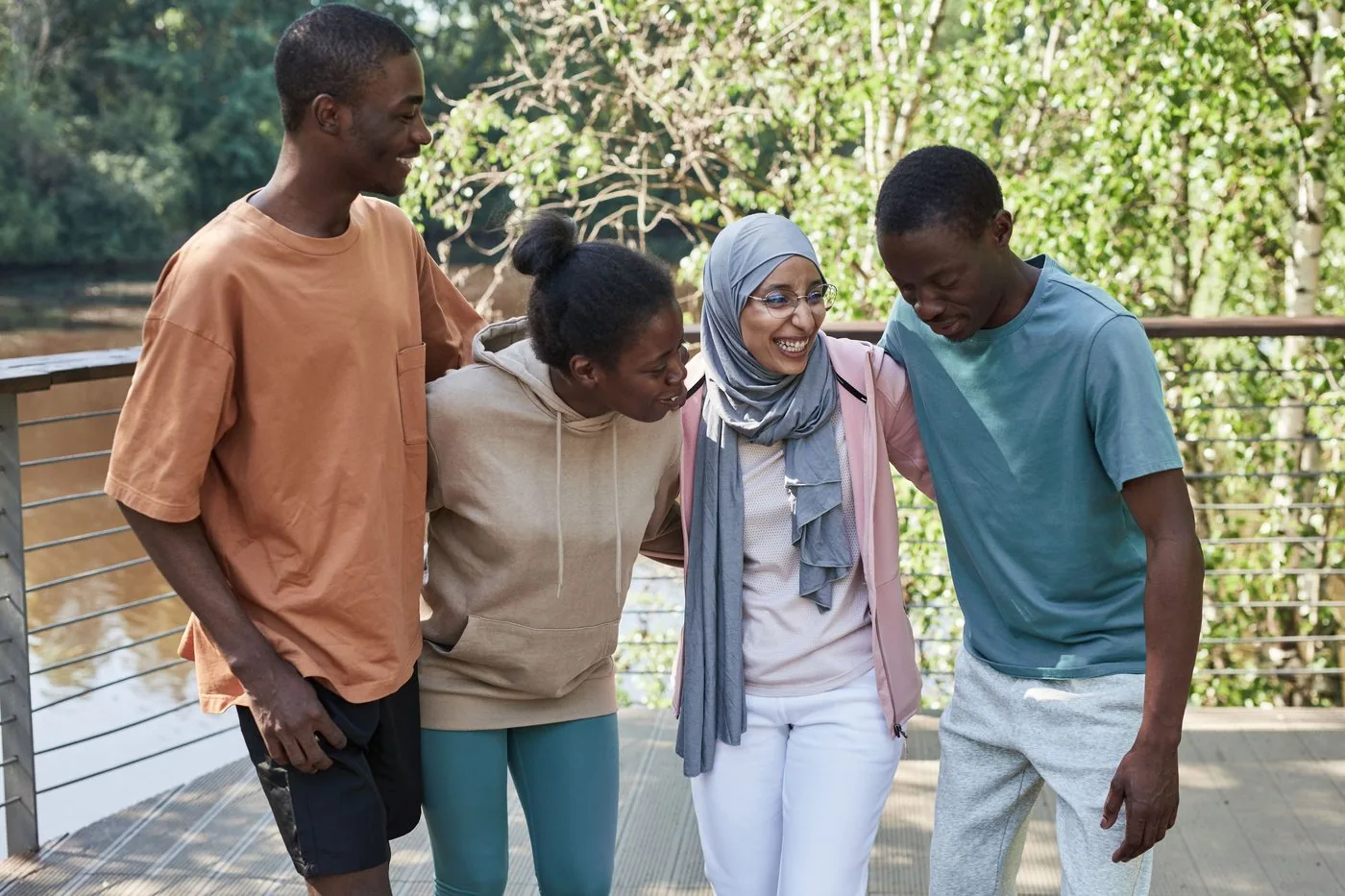 Four diverse friends laughing together outdoors, arms around each other